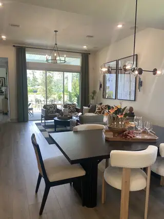 A modern living area with a sleek dining set, chic lighting, and large windows opening to a lush outdoor space.