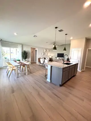 Open-concept living area with wood flooring, modern lighting, and a kitchen island, perfect for stylish entertaining.