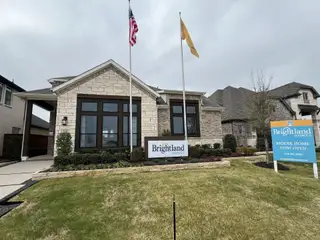 A stunning model home with a stone facade, large windows, and a manicured lawn in Solterra Texas by Brightland Homes (Mesquite, TX).