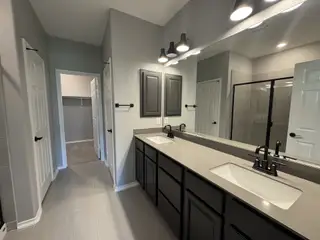 A sleek bathroom featuring dual sinks, modern fixtures, and a spacious shower, enhanced by stylish lighting.