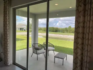 Model Home A serene patio view with cozy chairs and a small table overlooking lush greenery and a tranquil waterway.