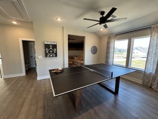 A recreational room with a sleek ping pong table, ceiling fan, and large windows offering ample natural light.