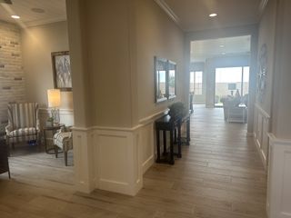 Model Home A bright hallway with elegant wood flooring, featuring cozy seating, stylish decor, and a view to a sunlit living room.