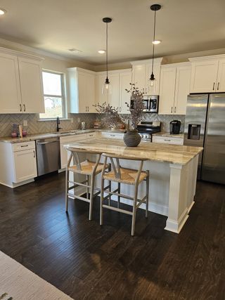 Model Home A modern kitchen with white cabinets, a stylish island, dark wood floors, and elegant pendant lighting.