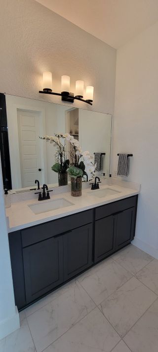 A contemporary bathroom featuring dual sinks, a sleek dark vanity, elegant lighting, and white tiled flooring.