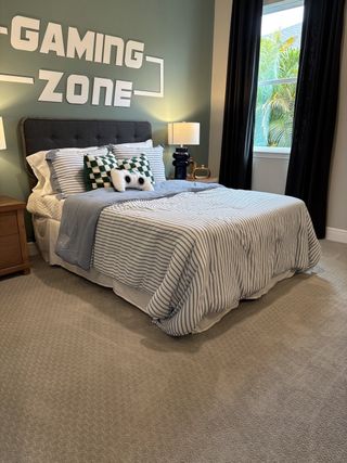 A cozy bedroom with a "Gaming Zone" wall feature, stripped bedding, plush pillows, and a verdant view from the window.