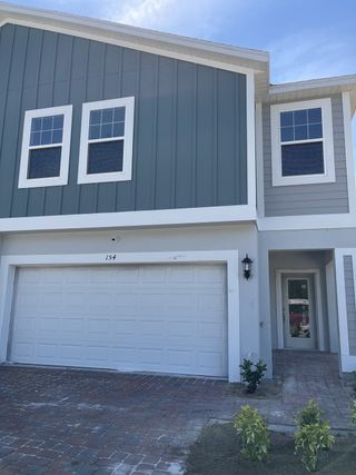 A modern gray townhome with a white garage and landscaped entry in Blue Springs Reserve Townhomes by Trinity Family Builders (Groveland, FL).