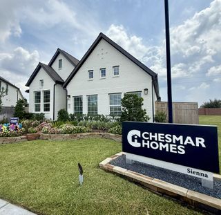 Model Home A charming white brick home with lush landscaping in Sienna by Chesmar Homes, Missouri City, TX.