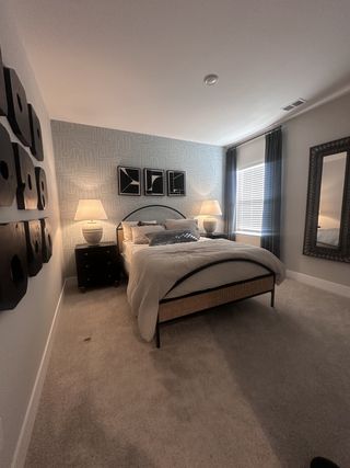 A cozy bedroom featuring patterned wallpaper, modern art, stylish lighting, and plush carpet for a comfortable ambiance.
