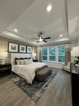 A serene bedroom with plush bedding, elegant wood floors, and large windows offering a scenic view.