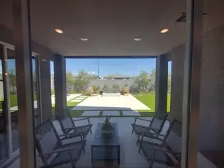 Model Home A cozy patio with stylish wicker chairs, a coffee table, and a view of the landscaped backyard featuring lush greenery and a paved area.