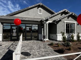 A Mediterranean-style house with brown shutters, a dark garage, and a paved driveway, set in a sunny neighborhood.