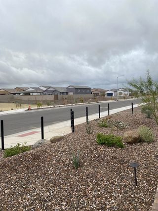 A gray, overcast day in Artisan at Asante (Surprise, AZ) by Taylor Morrison features modern homes along a street with desert landscaping and gravel ground cover.