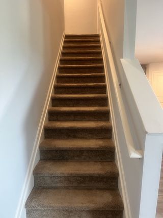 Carpeted staircase with modern railing and neutral walls, leading to an upper level in a cozy interior space.