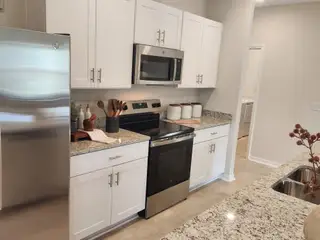 Street view A modern kitchen with sleek white cabinets, granite countertops, stainless steel appliances, and neutral tile flooring.