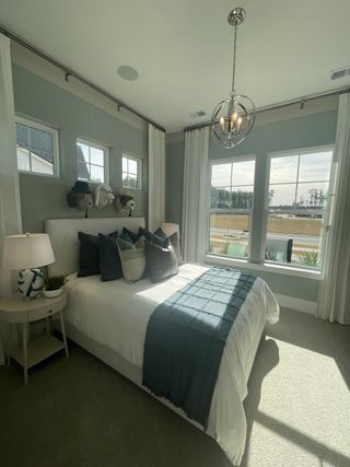 A cozy bedroom with elegant light grey walls, stylish bedding, and a modern chandelier illuminating the space.