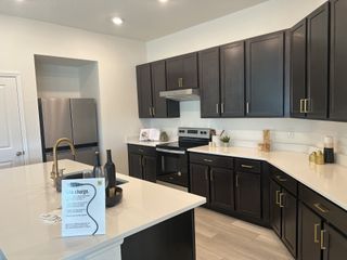 A modern kitchen with dark wood cabinets, sleek countertops, a stainless-steel fridge, and brass accents for a stylish touch.