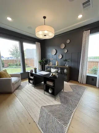 A modern home office with dark accent walls, large windows, and stylish decor, featuring a cozy seating area and sleek desk.