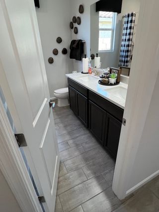 Model Home A modern bathroom with a sleek dark vanity, wall decor, tile flooring, and stylish checkered shower curtain.