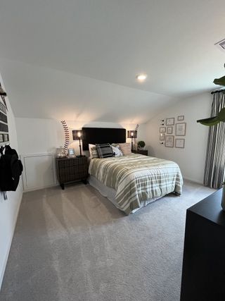 A cozy bedroom featuring a neatly made bed, soft carpeting, elegant wall art, and warm lighting creating a relaxed atmosphere.