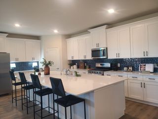 A modern kitchen with crisp white cabinets, sleek blue tile backsplash, and a spacious island with seating.