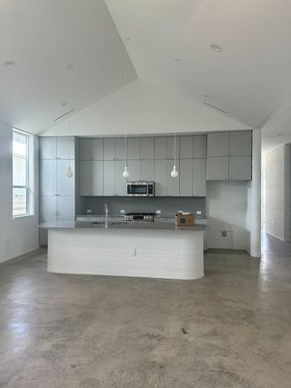 Model Home A modern kitchen with sleek grey cabinetry, concrete floors, and pendant lighting over a curved island.