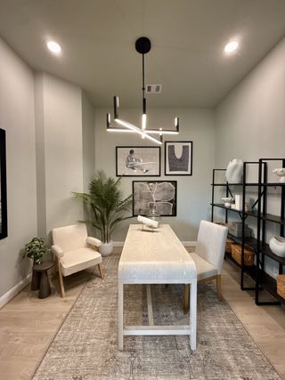 A modern home office with sleek lighting, a light wood desk, plush chairs, and minimalist decor.