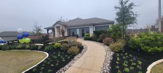 A charming model home in Remington Ranch by Meritage Homes (San Antonio, TX) with a stone and siding exterior, landscaped walkway, and festive balloons.