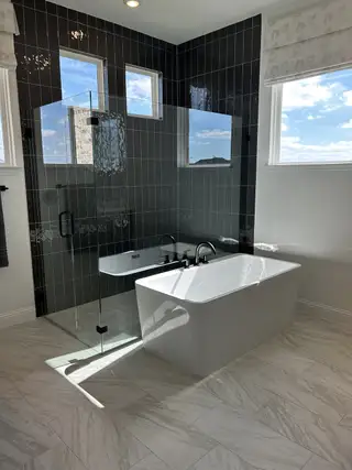 A luxurious bathroom featuring a sleek black-tiled shower, modern bathtub, and elegant marble flooring.