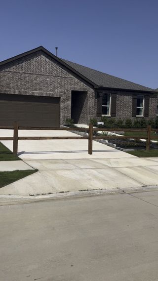 Street view A modern brick home with a rustic wooden fence in Heartland Signature by KB Home (Heartland, TX).
