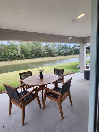 A serene patio with a round wooden table and chairs, overlooking a tranquil pond and lush greenery.