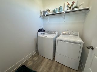 A bright laundry room with modern washer and dryer, light wood floors, and decorative shelving for added charm.