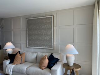 A cozy living room with paneled walls, a white sofa, abstract art, and soft lighting from elegant table lamps.