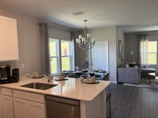 Model Home A modern, open-plan living area featuring a sleek kitchen, cozy dining space, and inviting lounge with large windows and elegant decor.