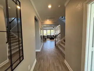 A welcoming hallway with wooden floors, elegant staircase, and bright living space beyond.