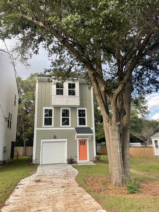 A charming green home with an inviting orange door and large tree in Rivers Edge by DRB Homes (North Charleston, SC).