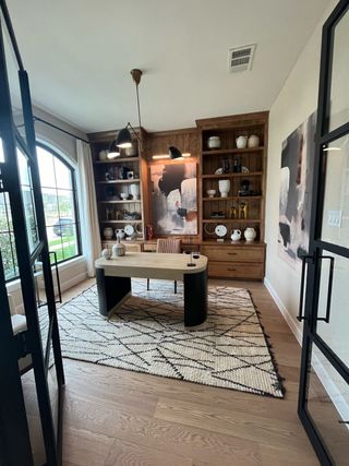A stylish home office with wooden shelves, modern desk, abstract art, and large window with natural light.