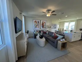 Modern living area with a plush gray sofa, abstract art, and an open kitchen and dining space. Cozy and inviting atmosphere.