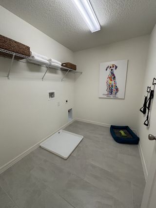A pet-friendly laundry room with tiled floors, a dog bed, bright lighting, and playful canine artwork.