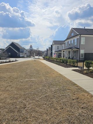 A peaceful neighborhood street features modern homes with varying facades, a paved sidewalk, and a central community building with a distinctive dome in Harmony by Kinglett Homes (Auburn, GA).