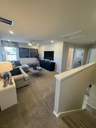 Model Home A cozy living room with a beige carpet, plush sofa, and modern decor. Stairs lead down, enhancing the open and inviting space.