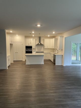 A modern kitchen with sleek white cabinets, a central island, and elegant wood flooring.