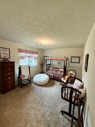 Model Home A cozy nursery with a wooden crib, plush seating, soft carpet, and warm lighting. Perfect for a soothing and welcoming space.