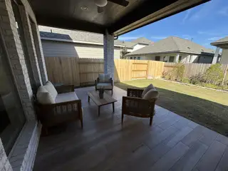 A cozy, covered patio with modern seating and a view of the fenced backyard.