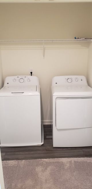A convenient laundry room with modern white washer and dryer, featuring ample shelving and a cozy carpeted floor.