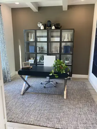 A sleek home office with a bold black desk, glass cabinetry, and warm accent walls for a sophisticated workspace.