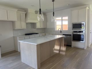A modern kitchen with white cabinetry, quartz countertops, and pendant lights over a central island.