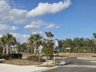 A sunny day view in Cross Creek by D.R. Horton (Green Cove Springs, FL) features palm trees, community signage, and a glimpse of recreational areas.