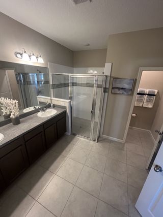 Model Home A modern bathroom with a double sink vanity, glass shower, and sleek tile flooring, complemented by neutral tones.