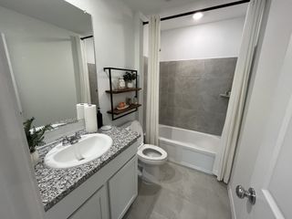 A stylish bathroom with a granite countertop, modern fixtures, and a shower with tiled walls.